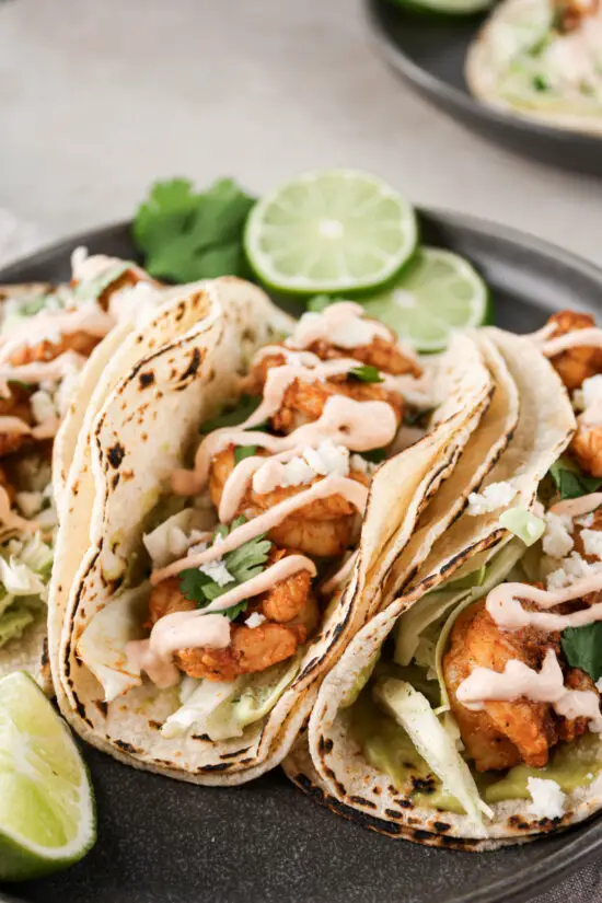 Spicy shrimp tacos with fresh lime slices and cilantro leaves.