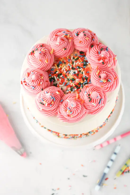Swirls of pink buttercream frosting on top of gluten-free funfetti cake.