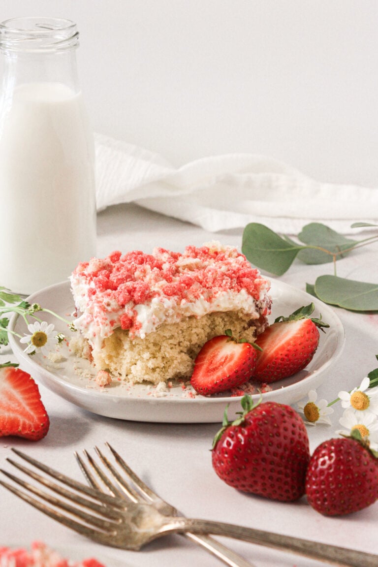 Slice of gluten-free strawberry crunch poke cake topped with whipped cream and fresh strawberries.