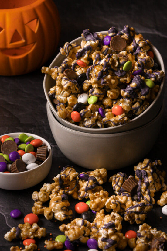 Bowl filled with Halloween Caramel Corn and jack o' lantern pumpkin in background.