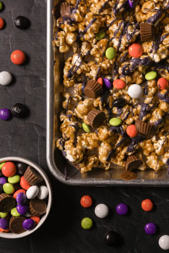 Cookie tray filled with Halloween Caramel Corn and scattered chocolate coated candies all around. 