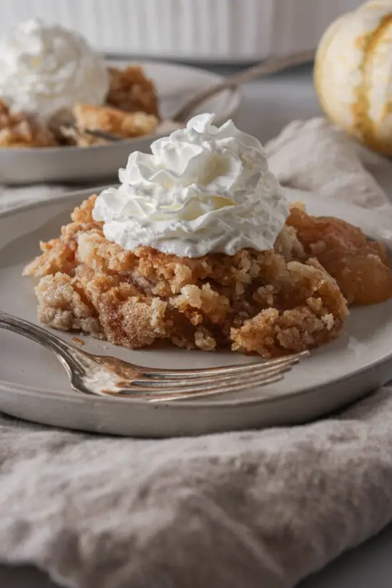 Slice of Caramel Apple Dump Cake on a plate with whipped cream on top. 