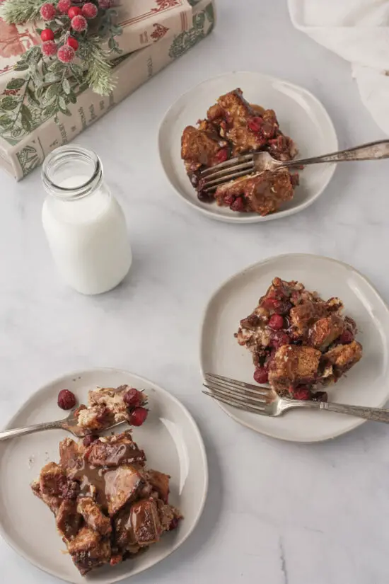 Three plates filled with holiday cranberry French toast bake and a glass of milk. 