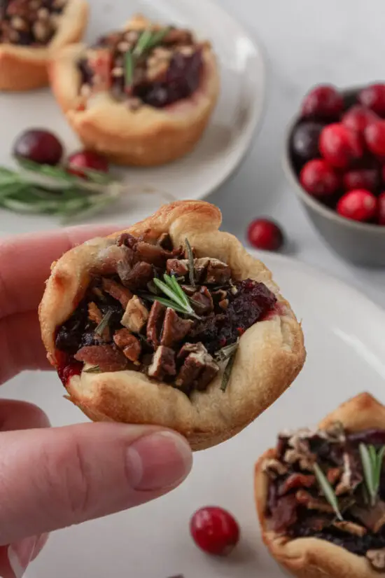 Hand holding a single Cranberry Brie Bite with fresh sprig of rosemary on top.