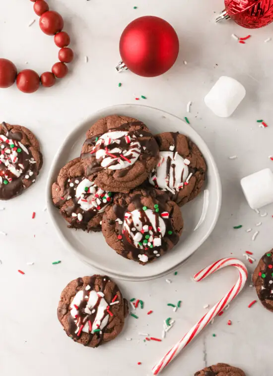 Hot chocolate cookies stacked on a plate with marshmallows and candy cane. 