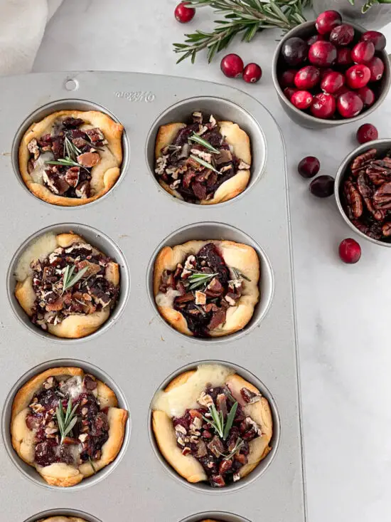 Muffin pan filled with Cranberry Brie Bites and fresh cranberries. 