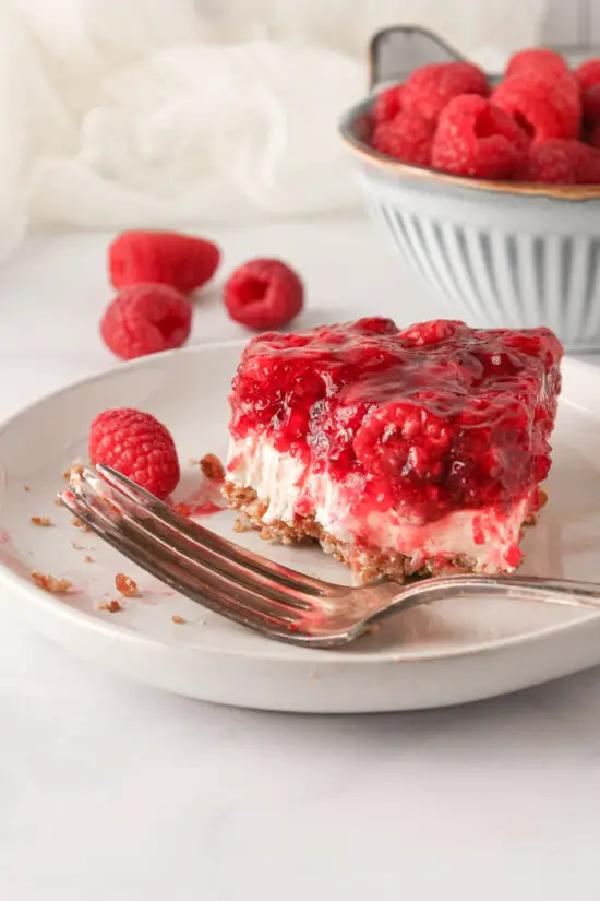 Slice of Raspberry Pretzel Salad on a small plate with fork and fresh raspberries to the side. 