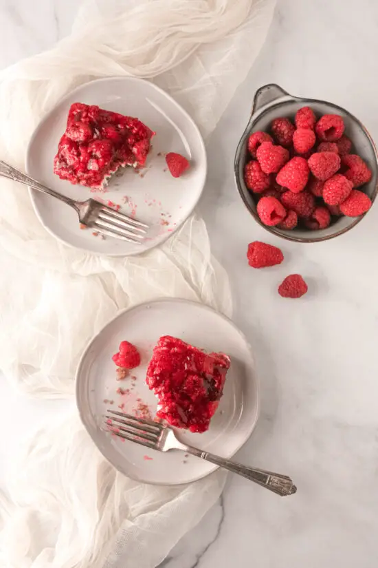 Two slices of Raspberry Pretzel Salad on dessert plates with bowl of fresh raspberries nearby.