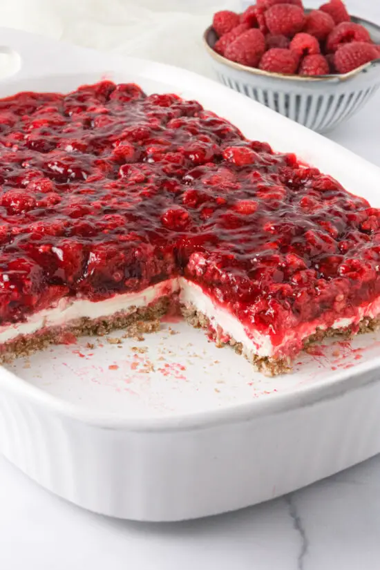 Baking pan half filled with Raspberry Pretzel Salad and bowl filled with fresh raspberries. 