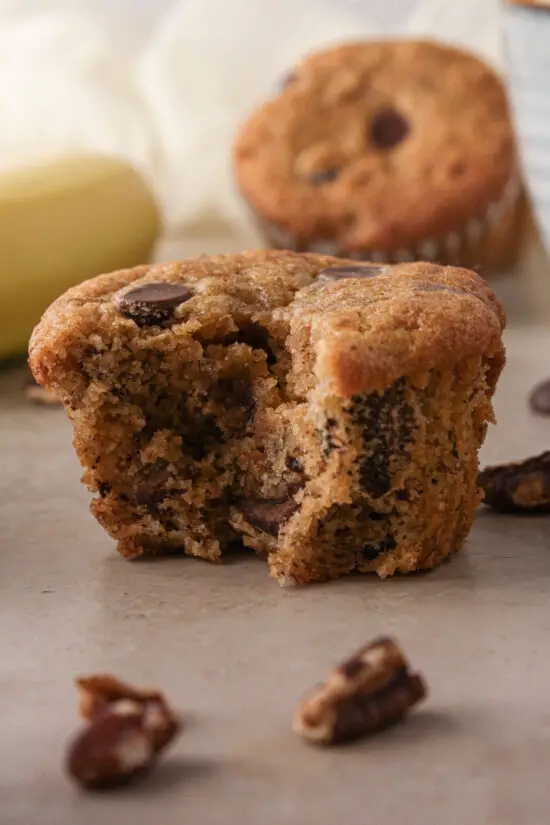 Bite taken out of an up close picture of a Banana Chocolate Chip Muffin. 