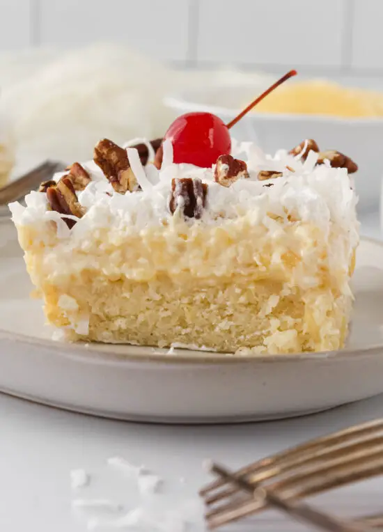 Slice of Gluten-Free Hawaiian Dream Cake with shredded coconut, pecans, and a cherry on top. 