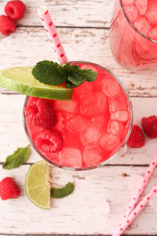 Large up-close glass of Raspberry Limeade with crushed ice and fresh raspberries, lime wedge and fresh sprig of mint. 