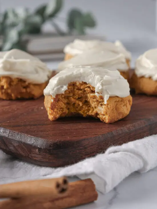 Wooden board with a bit taken out of a Soft Pumpkin Cookie with Cream Cheese Frosting. 