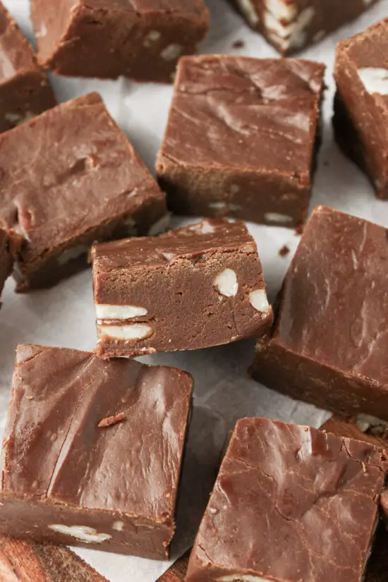 Square pieces of Easy Chocolate Pecan Fudge scattered over wooden board.