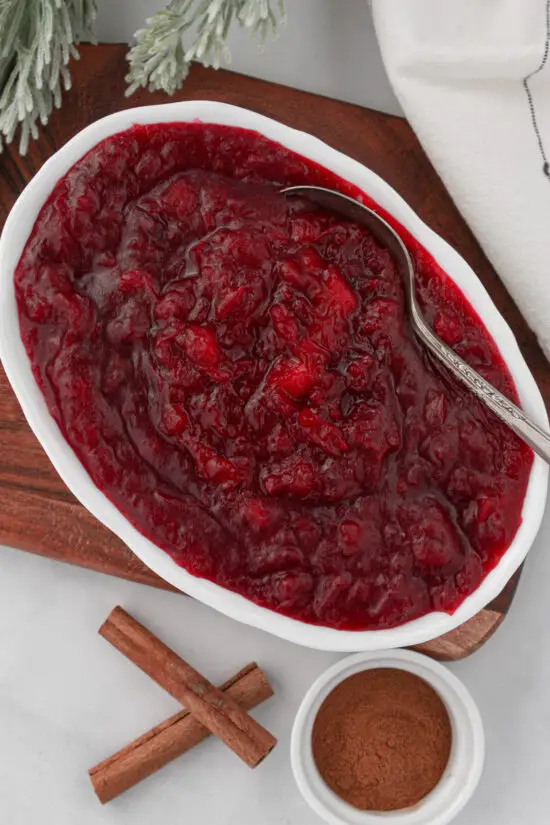 Dish filled with Apple Cranberry Sauce with spoon and cinnamon sticks.
