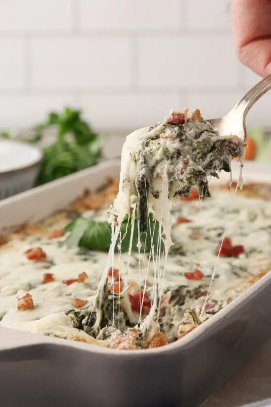 Spoon filled with Cheesy Bacon Spinach Dip and cheese pull. 