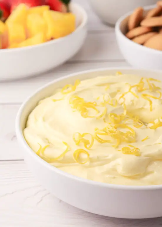 Bowl filled with Easy Lemon Fruit Dip with side of fruit and vanilla wafer cookies.