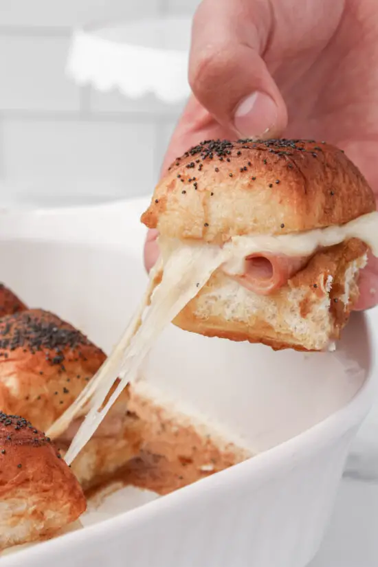 Hand holding a Hawaiian Ham and Cheese Slider with melted cheese coming out the side. 