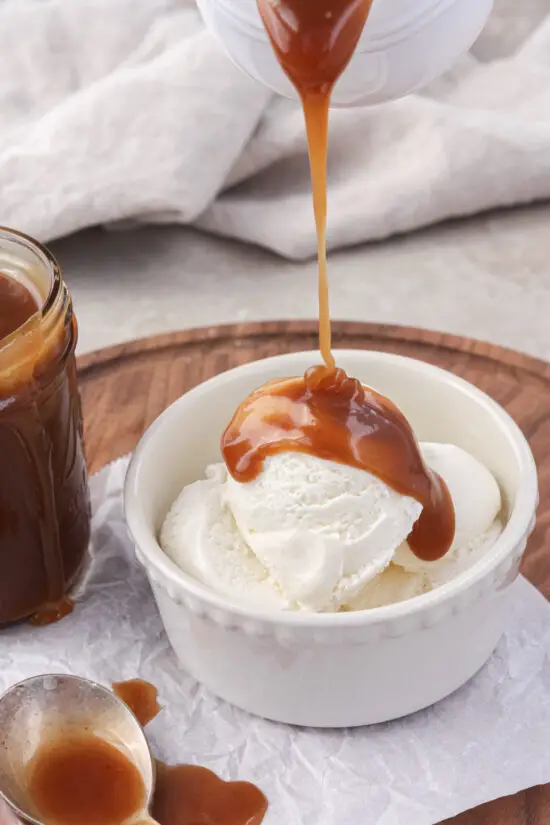 Brown Sugar Caramel Sauce being poured over a bowl of vanilla ice cream. 