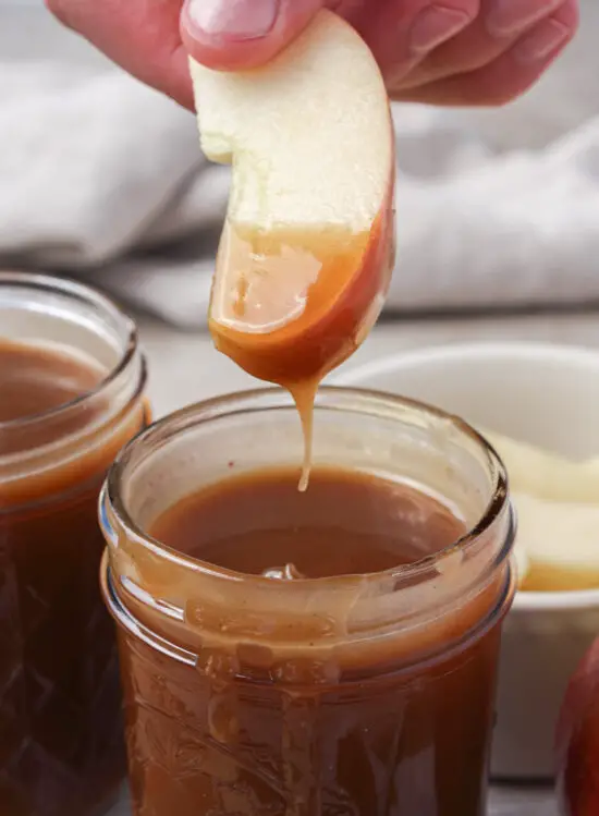 Apple slice dipped into jar of Brown Sugar Caramel Sauce. 
