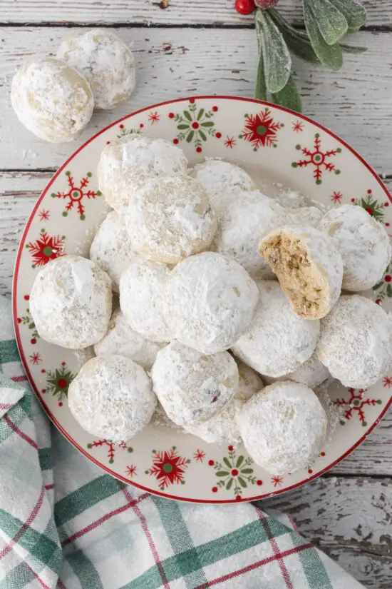 Plate filled with Classic Christmas Snowball Cookies with a bite taken out of one.