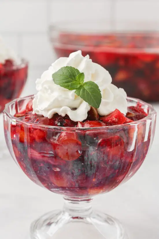 Individual glass bowl with Easy Raspberry Jello Fruit Salad Recipe and whipped cream on top. 