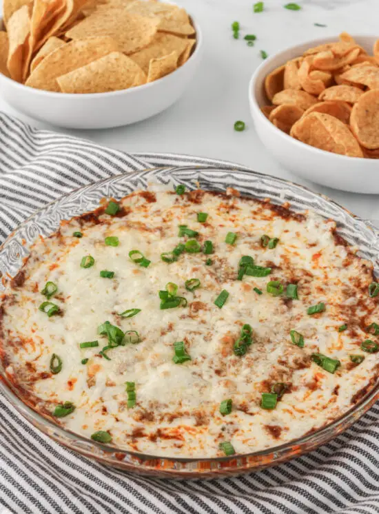 Cheesy Chili Cheese Dip garnished with green onions in a glass dish.