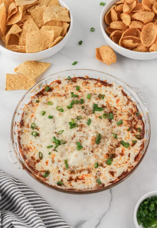 Chili Cheese Dip in a glass pie dish with corn tortilla chips on the side.